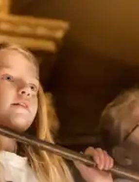 Två personer med suddade ansikten står bakom ett räcke inomhus, omgivna av varma toner.