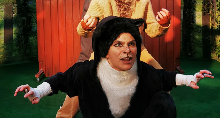 Tre personer i kattkostym poserar framför ett plank