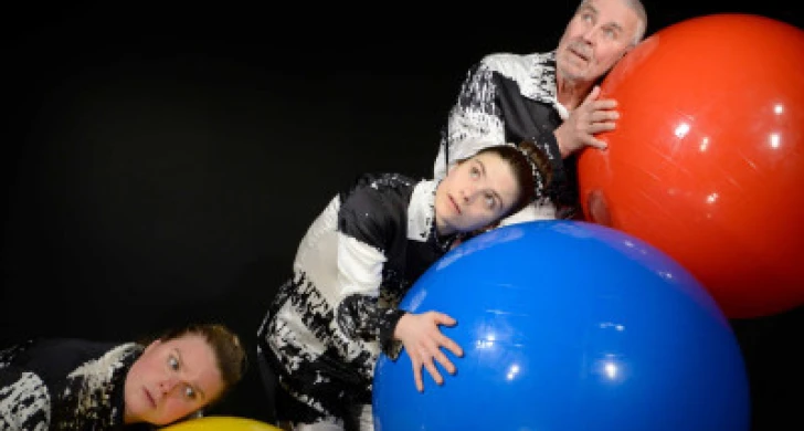 tre personer lutar sig mot och lyssnar på varsin stor boll i olika färger