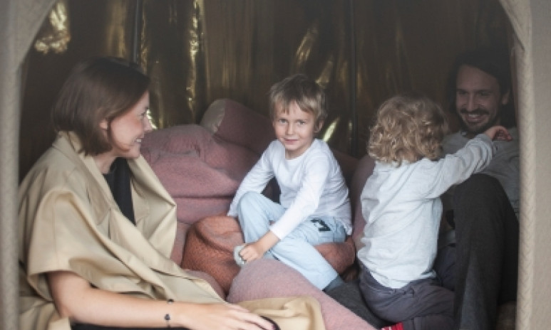Två vuxna och två barn sitter i en guldig hydda bland kuddar