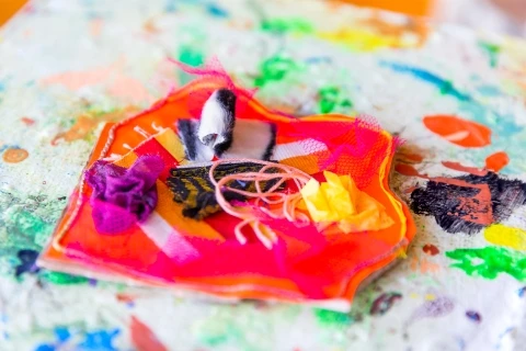 Handarbete av tygbitar, trådar och annat material i olika färger.