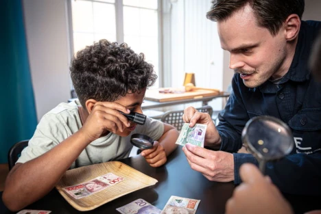 Pojke som undersöker sedlar tillsammans med en pedagog
