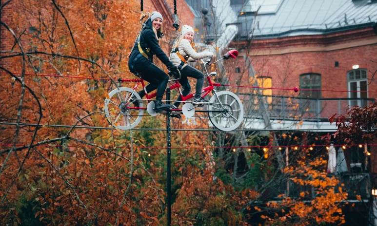 mamma och dotter cyklar på tandemcykel på en lina högt upp i luften