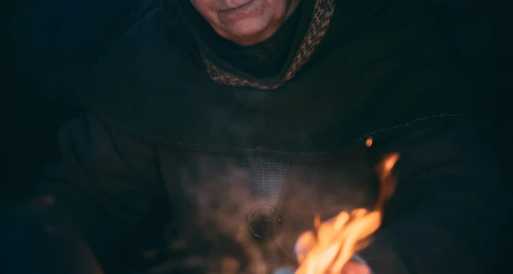 Kvinna i vikingatida kläder sitter vid en eld