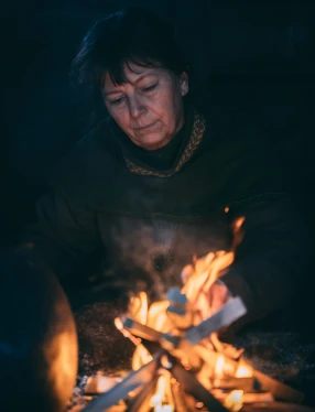 Kvinna i vikingatida kläder sitter vid en eld