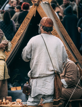En man i vikingatida kläder står framför ett vikingatält.