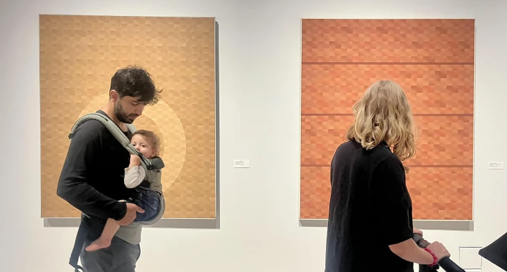 Föräldrar med barn i bärsele som tittar på konst.