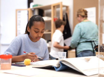 Ett barn som sitter vid ett bord och håller en penna i handen.