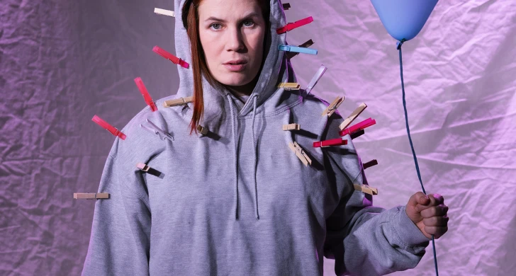 Lily iklädd grå luvtröja håller i en blå ballong. På luvtröjan finns många klädnypor fastsatta.