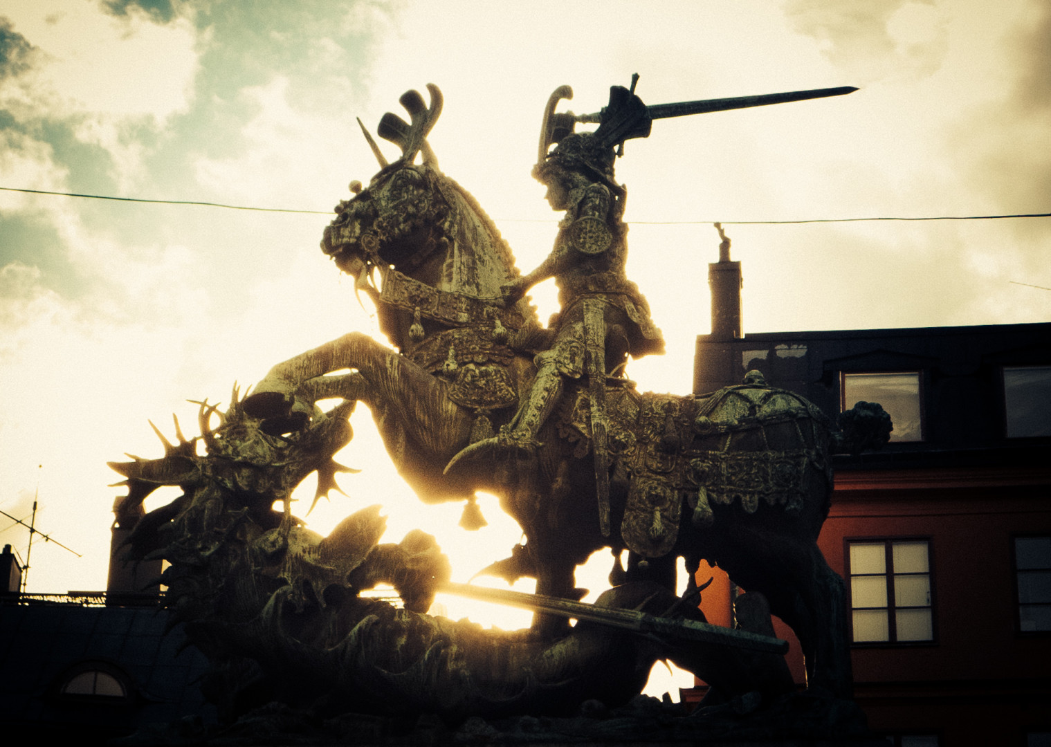 Riddare med höjt svärd på en stegrande häst dräper en liggande drake.
