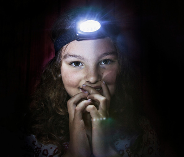 Barn med pannlampa i ett mörkt rum.