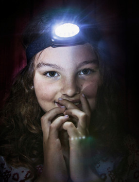 Barn med pannlampa i ett mörkt rum.