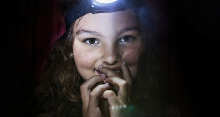 Barn med pannlampa i ett mörkt rum.