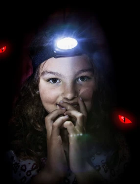 Flicka som tittar in i kameran med pannlampa på huvudet. Röda ögon syns i bakgrunden