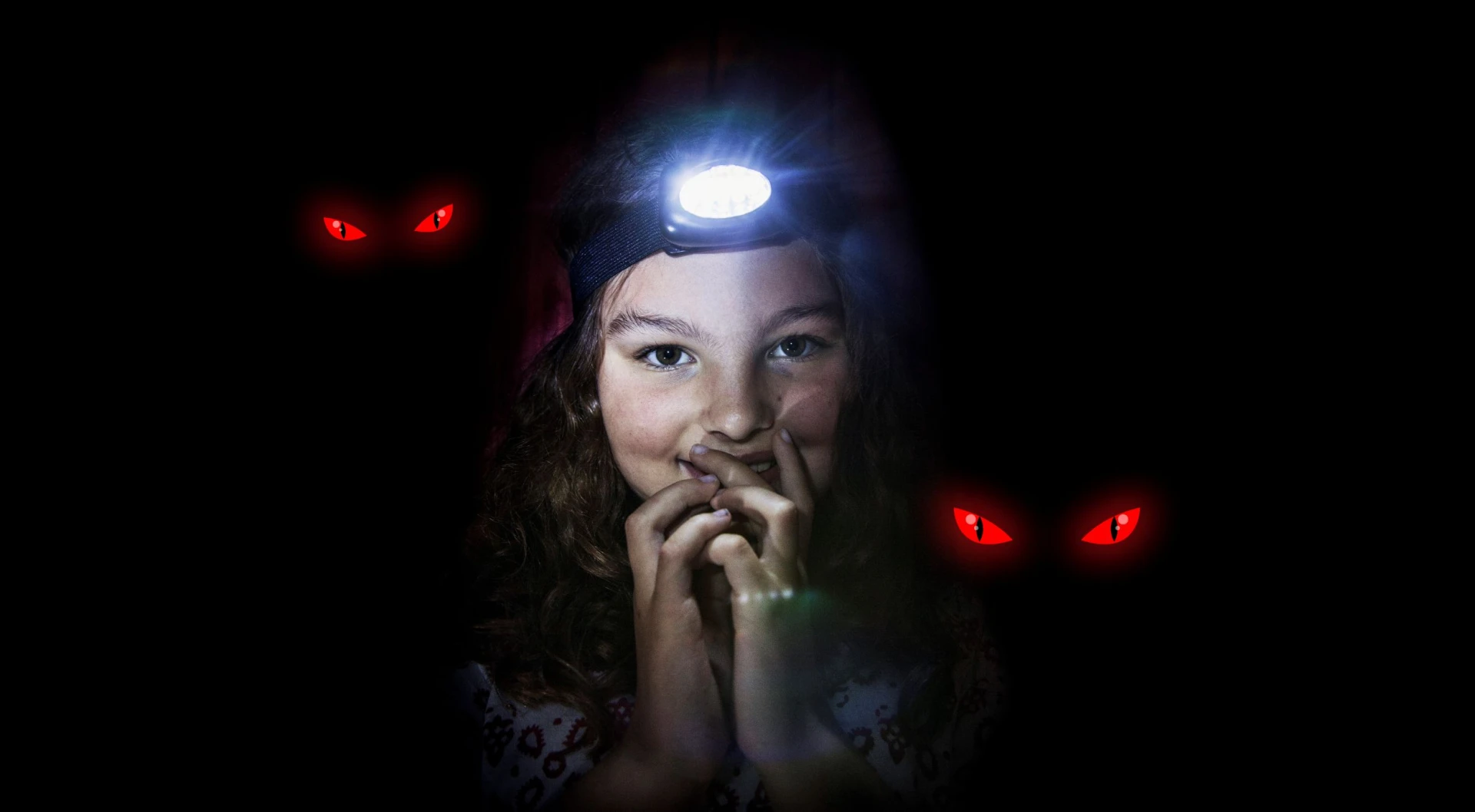 Flicka som tittar in i kameran med pannlampa på huvudet. Röda ögon syns i bakgrunden