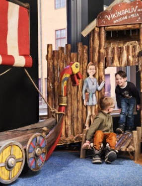Barn leker vid ett vikingaskepp och bryggor inomhus.