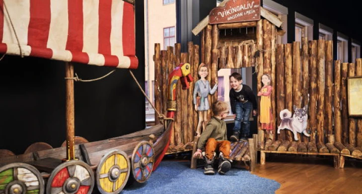 Barn leker vid ett vikingaskepp och bryggor inomhus.
