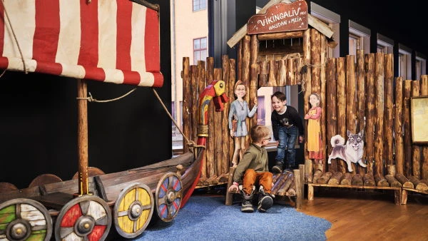 Barn leker vid ett vikingaskepp och bryggor inomhus.